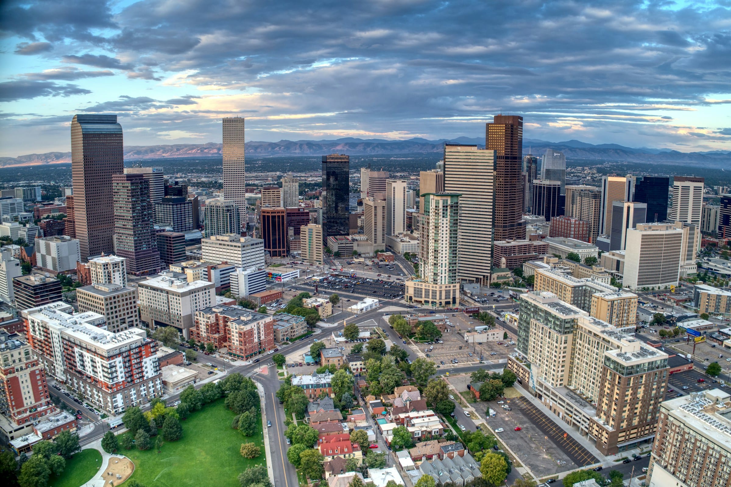 Downtown Denver skyline at dusk seen from above, with the Front Range on the horizon