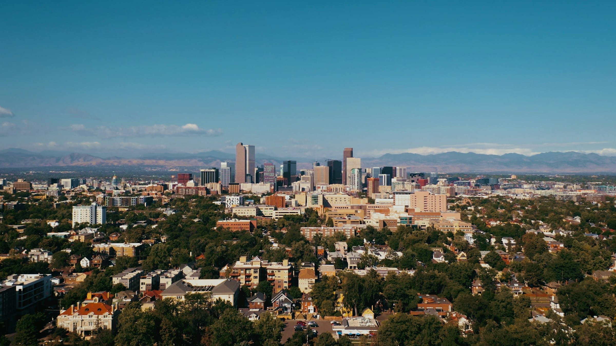 Aerial view of downtown Denver with residential neighborhoods in the foreground and the Rocky Mountains behind