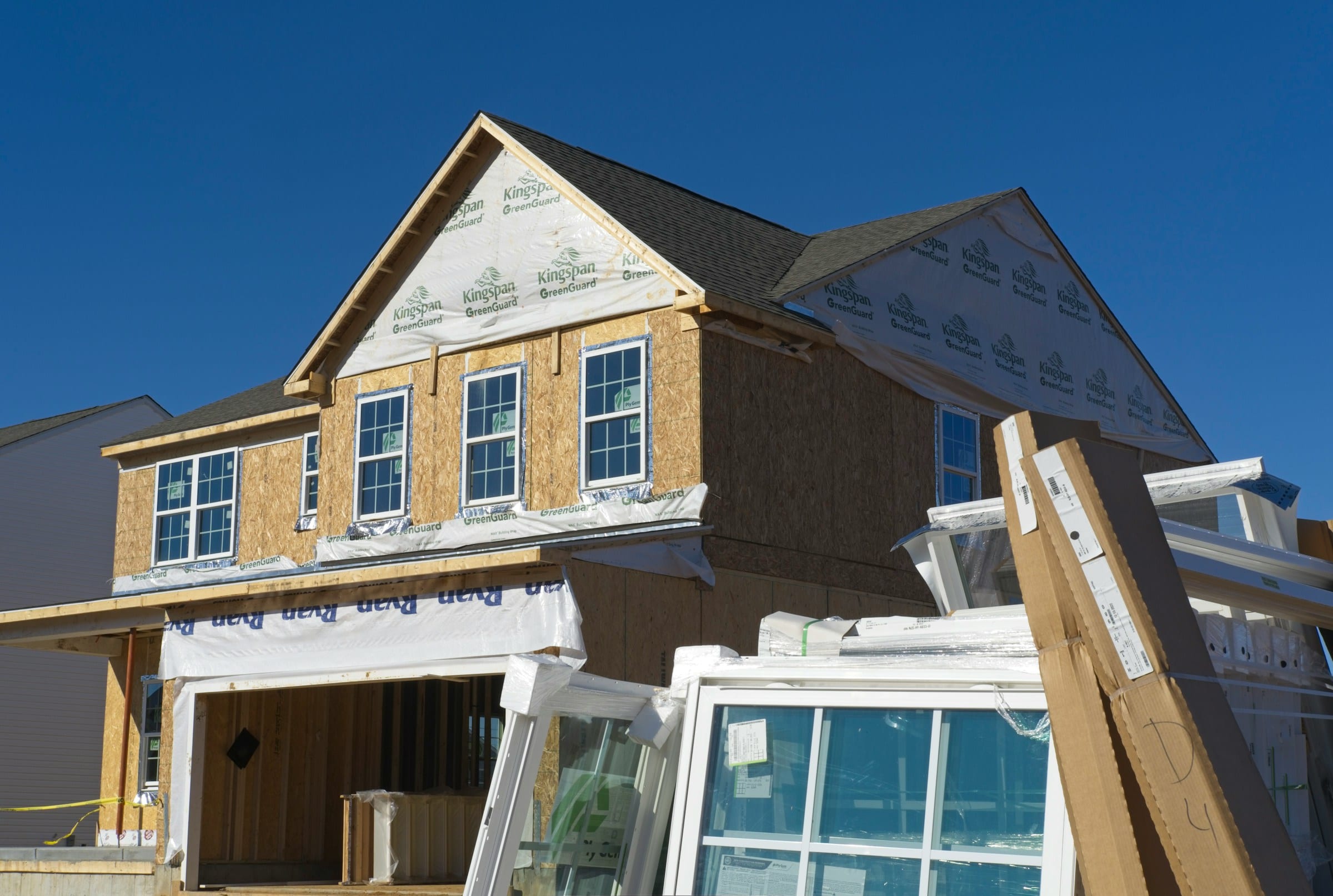 A new home under construction with sheathing in place and windows stacked ready to install