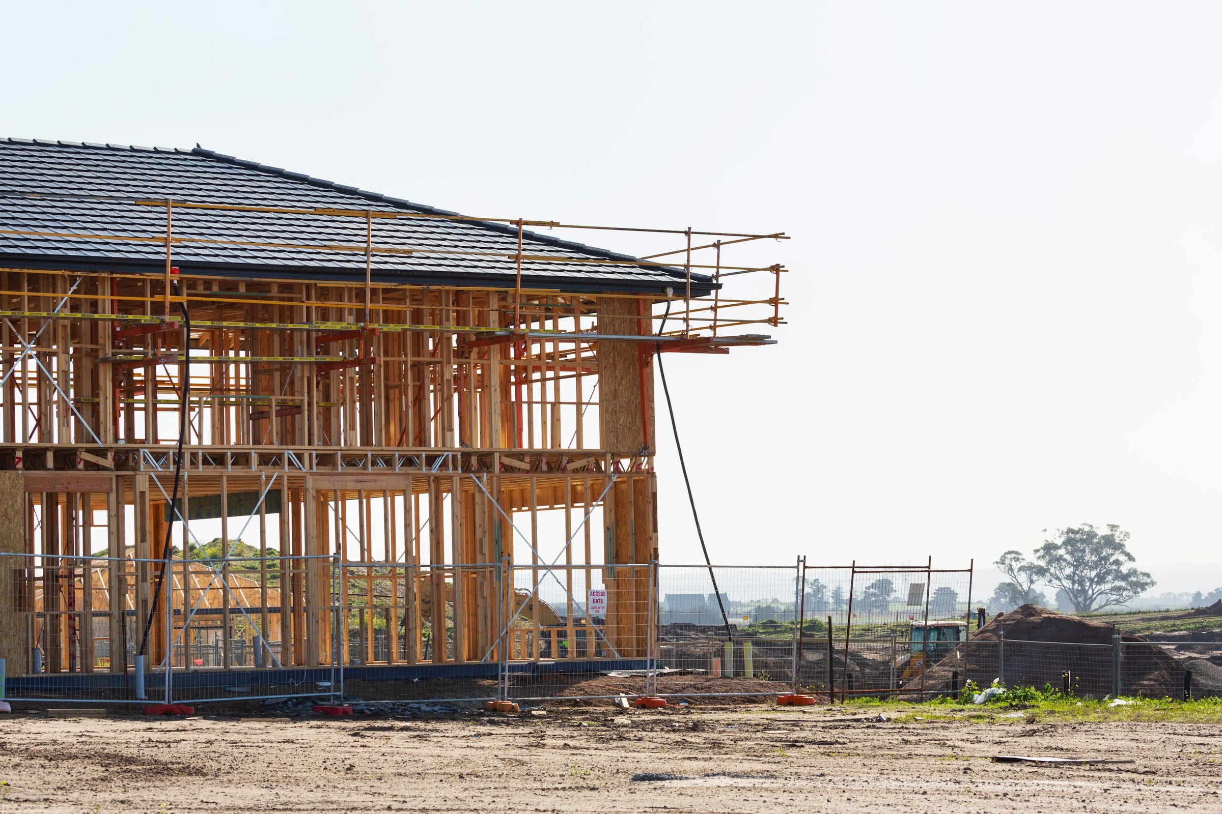 A two-storey home at the framing stage with scaffolding, on an open development site