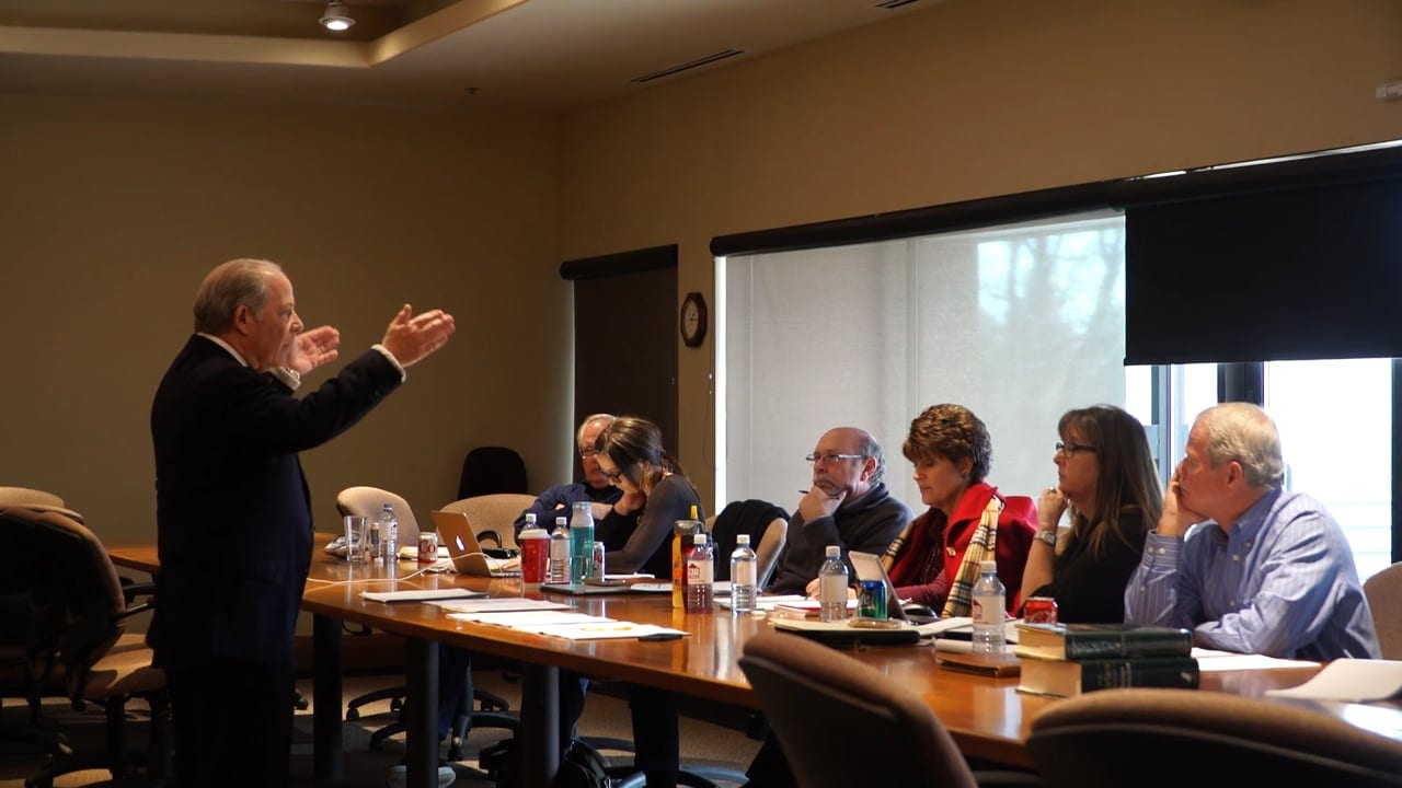 S. Robert August presenting to a group around a boardroom table
